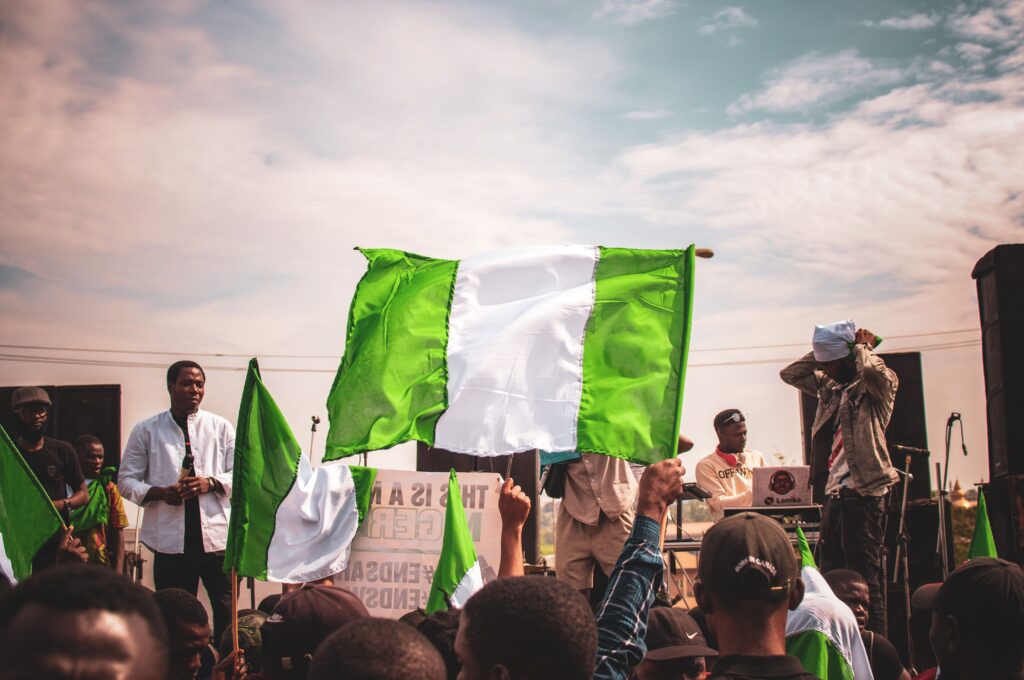 A vibrant gathering of people holding Nigerian flags outdoors under a sunny sky.
